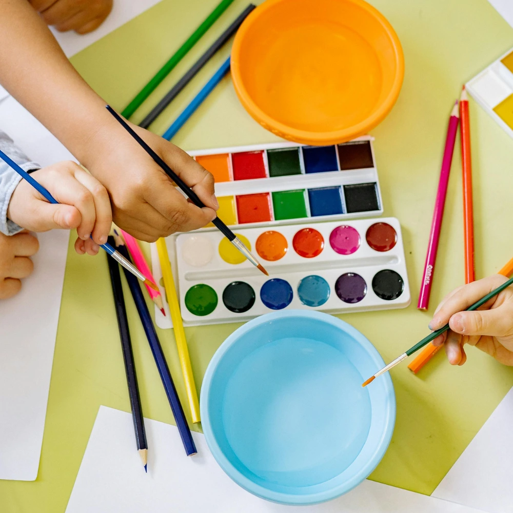 Children and adult's hands holding paintbrushes and dipping them into colourful paints.